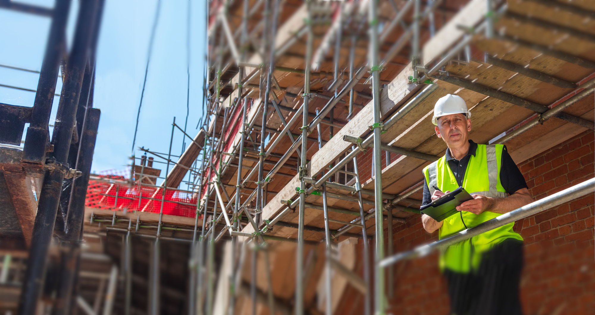 A man in a hard had standing under scaffolding.